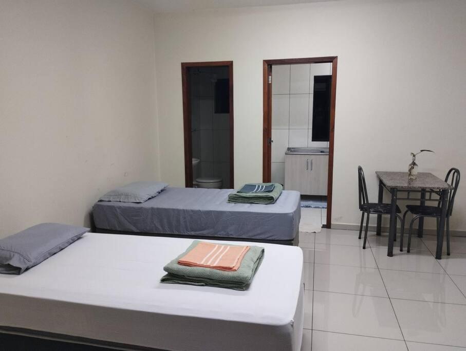 twee bedden in een kamer met een tafel en een keuken bij Kitnet 3 - Estada do Conforto in Guaíra