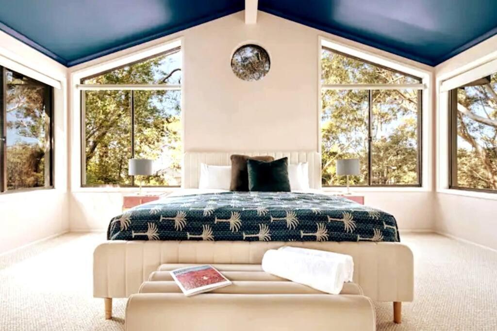 a bedroom with a bed and a couch and windows at Canto do Sol - 4BR Avoca Getaway in Avoca Beach
