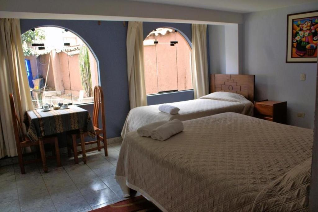 1 dormitorio con 2 camas, mesa y 2 ventanas en Samay Wasi Pisac Retreat, en Písac