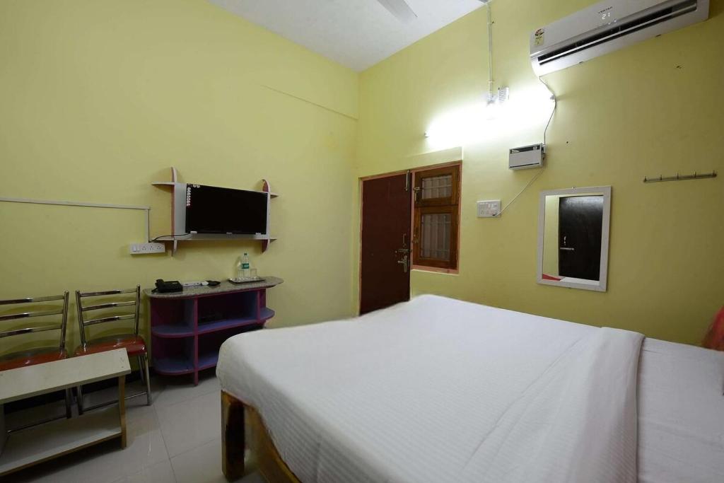 een slaapkamer met een bed, een bureau en een televisie bij THARAN Residency in Vellore