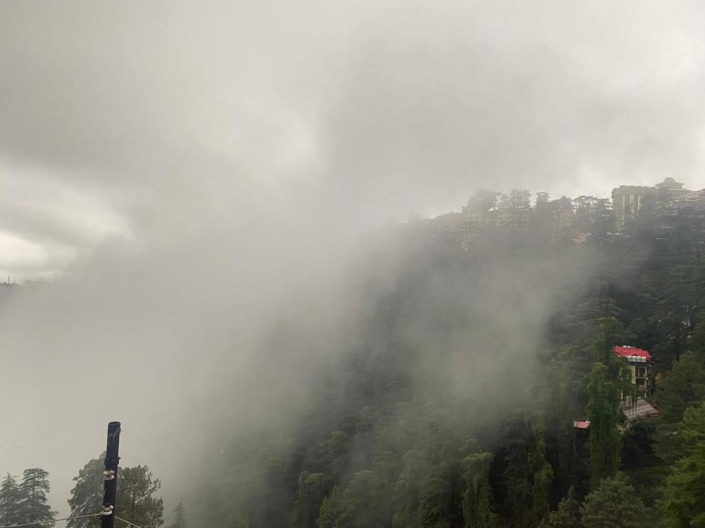 a misty mountain with trees and buildings in the background at Cozy Cove - Newly built 3BHK Duplex with rare valley view in Shimla
