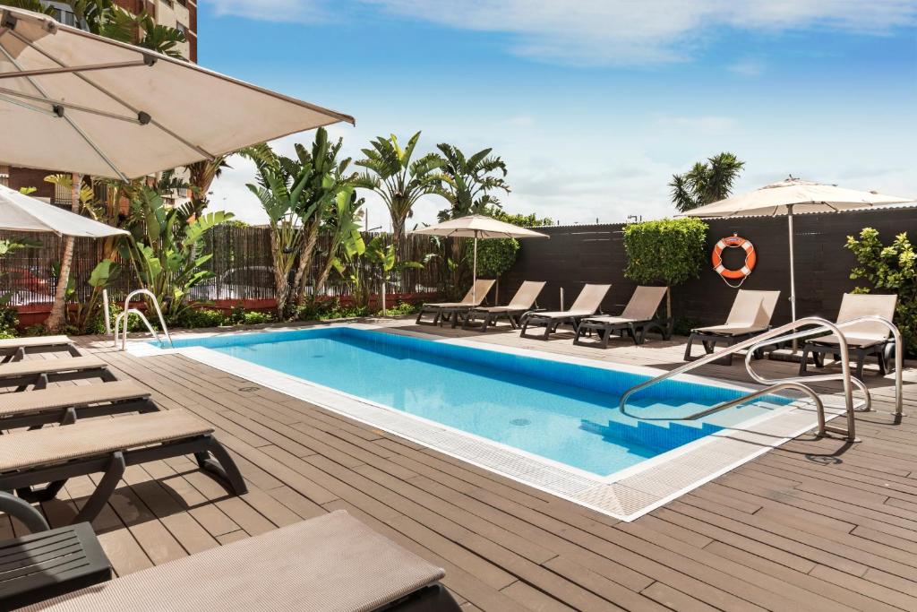 - une piscine avec des chaises et des parasols sur une terrasse dans l'établissement Catalonia Hispalis, à Séville