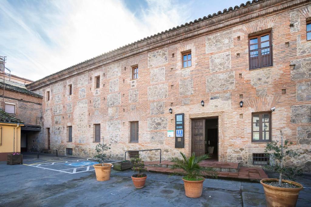 un grande edificio in mattoni con piante in vaso in un cortile di Hospedería Valle del Ambroz a Hervás