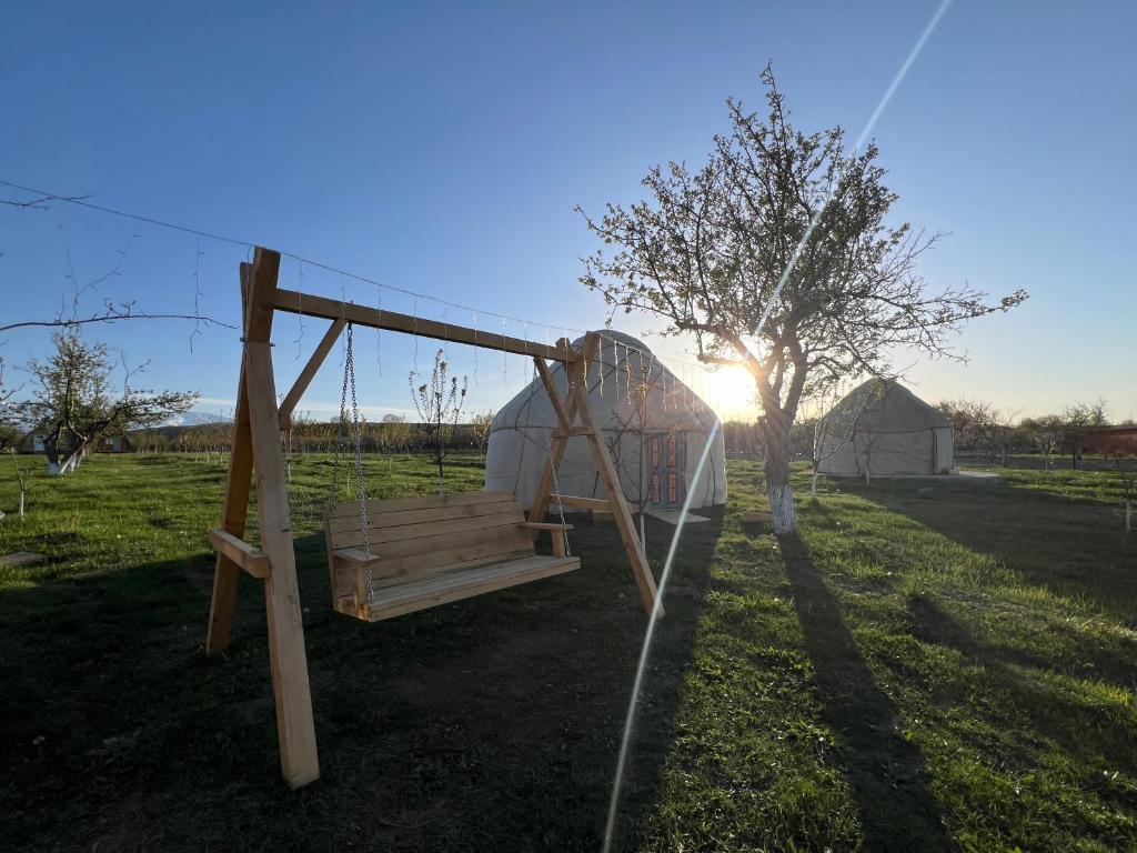 a wooden swing in a field with the sun setting at Bosogo Yurt camp in Bokonbayevo