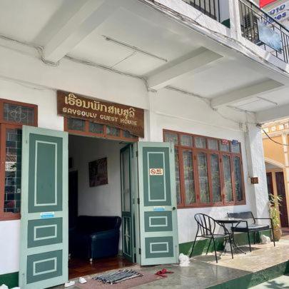 Saysouly Guest House في Ban Nongdouang: مبنى بأبواب خضراء وطاولة وكرسي
