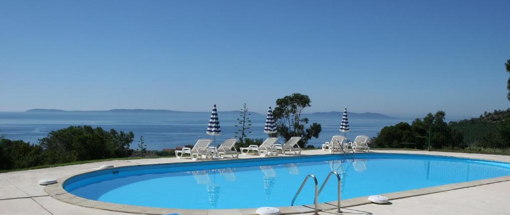 a swimming pool with chairs and the ocean in the background at Azur Hotel in Le Lavandou