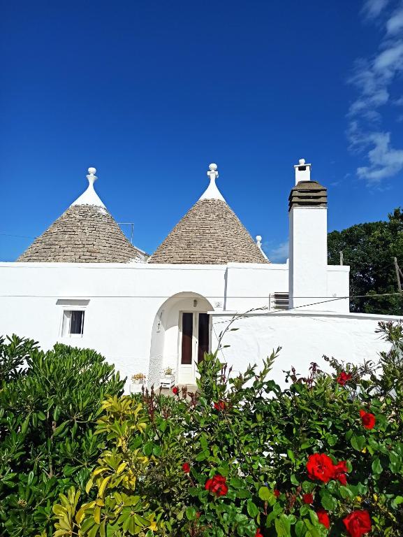a white house with two turrets and red flowers at Trullo in piena valle d'itria del 1800 in Cisternino