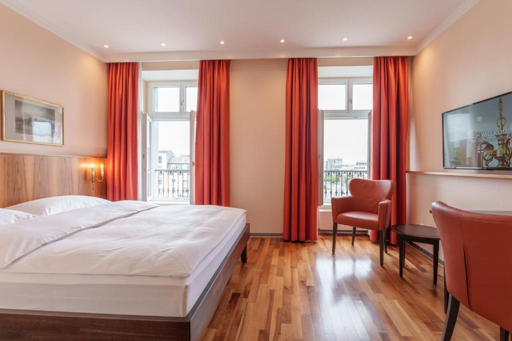 a bedroom with a large white bed and red curtains at Hotel Schweizerhof Basel in Basel