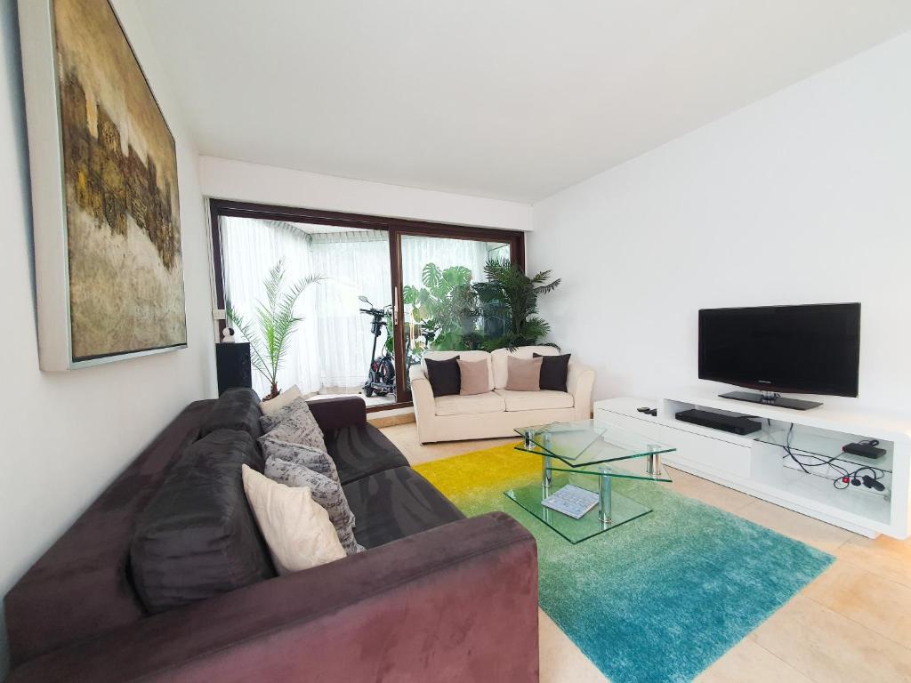 een woonkamer met een bank en een flatscreen-tv bij EXIGEHOME - Bel appartement à 500 m des JOs équitation - Piscine et tennis in Le Chesnay