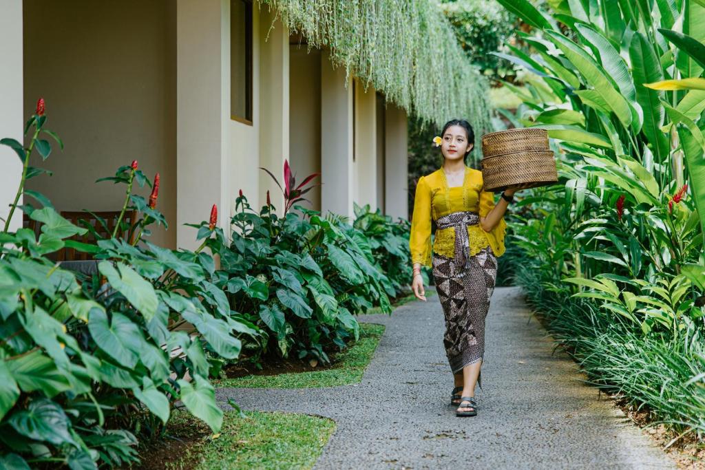 a woman walking down a path in a garden at Jati Cottage in Ubud