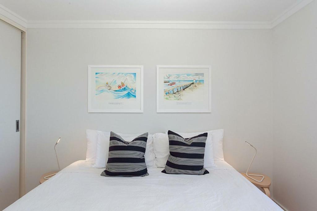 a white bedroom with a bed with two pillows at Ocean view Clovelly in Sydney