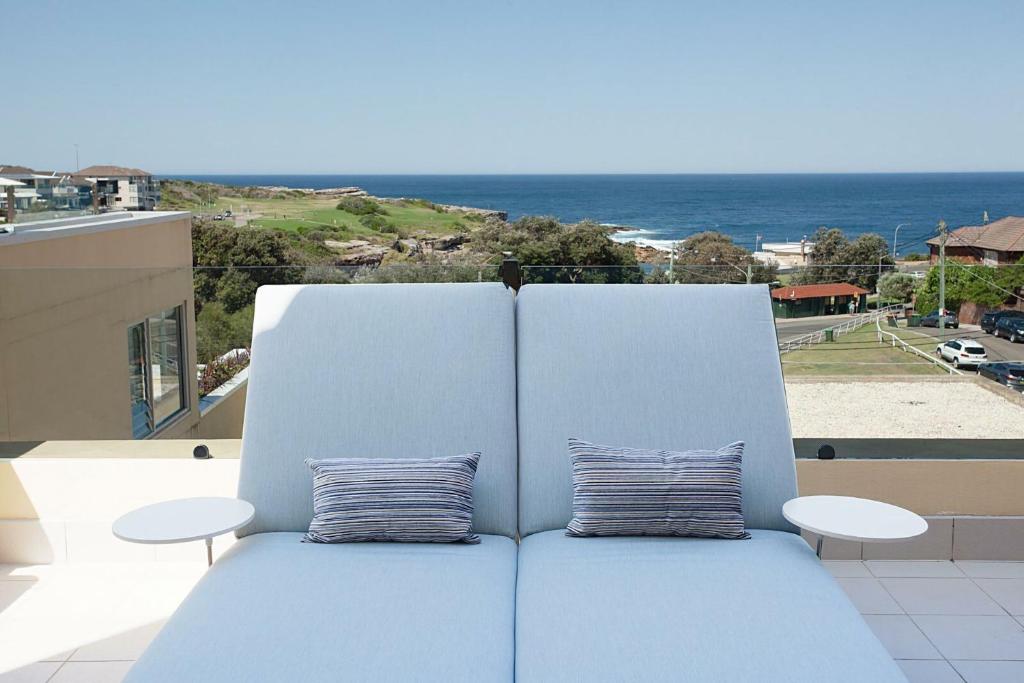 a blue couch sitting on top of a balcony with the ocean at Ocean view Clovelly in Sydney