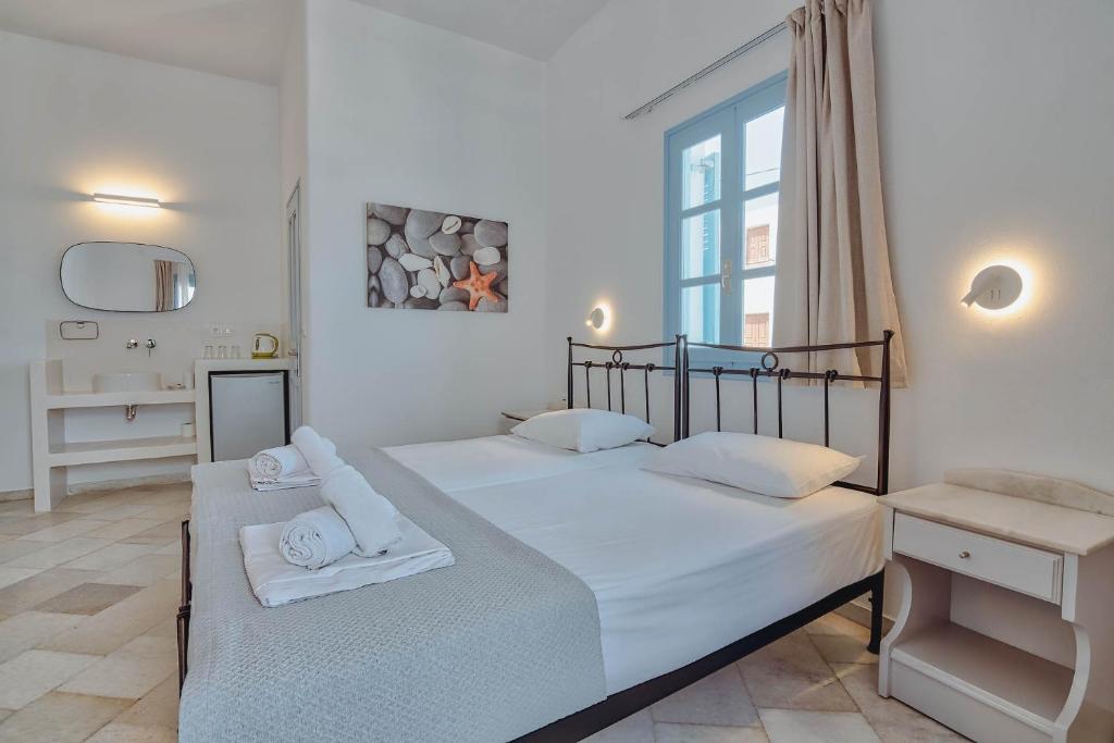 two beds in a white bedroom with a window at Hotel Mantalena in Antiparos Town