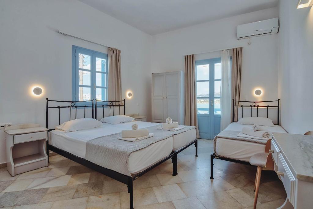 two beds in a bedroom with two windows at Hotel Mantalena in Antiparos Town