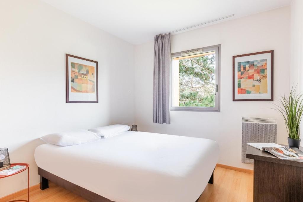 Appart'City Classic Nantes - Carquefou في كاركفو: غرفة نوم بيضاء بها سرير ونافذة