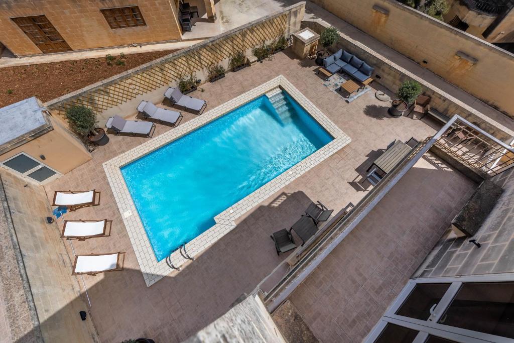 Tranquil Mansion - 3 Bed, Pool, BBQ & Gaming Room في Is-Swieqi: اطلالة علوية على مسبح مع كراسي وكراسي