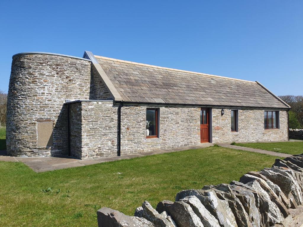 een stenen gebouw met een rode deur en een stenen muur bij Woodwick Mill Cottage in Evie