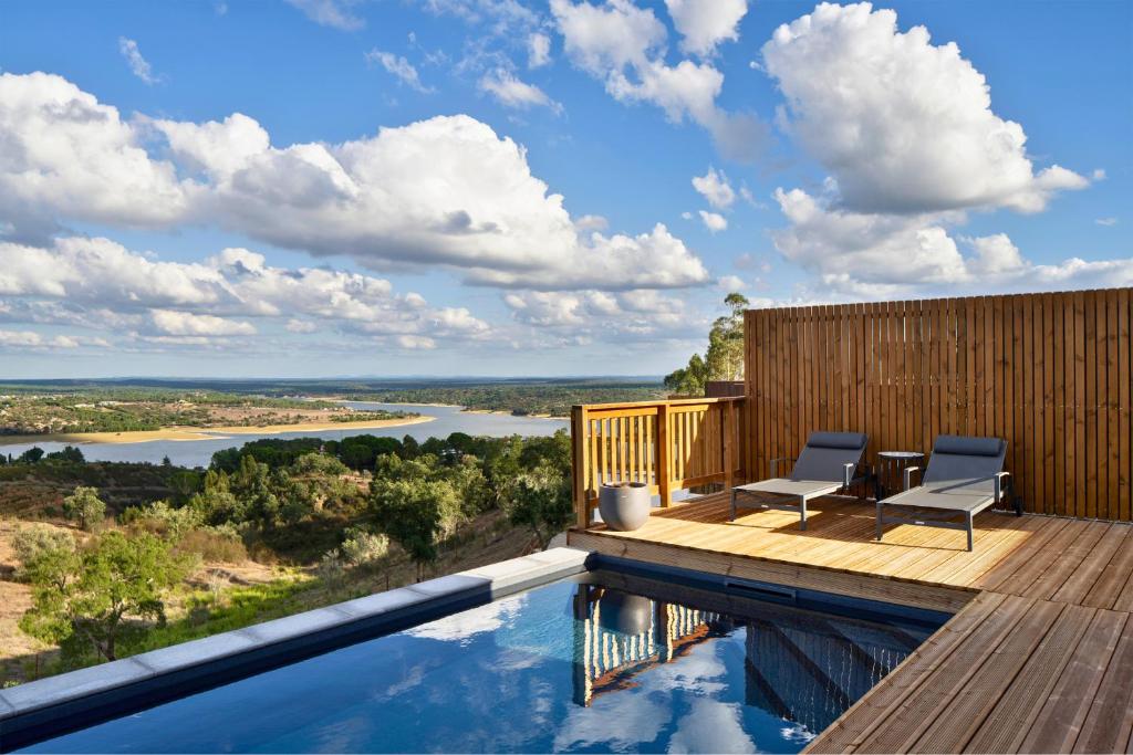 a pool with two chairs on a deck with a view of a river at Caju Villas Montargil - Villa Farinha Branca in Montargil