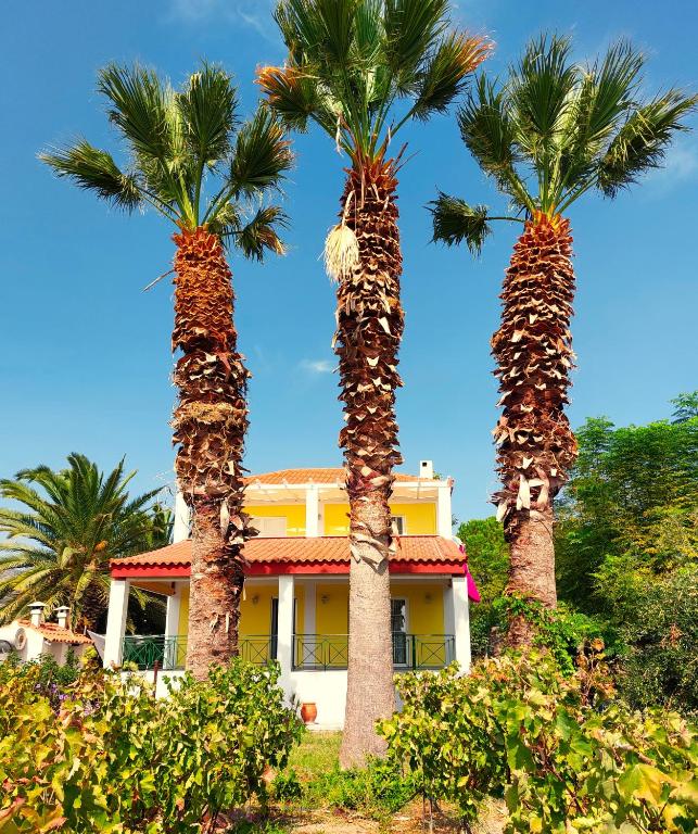 two palm trees in front of a yellow house at The Three Palms Samos Seaside Villa in Mesókampos