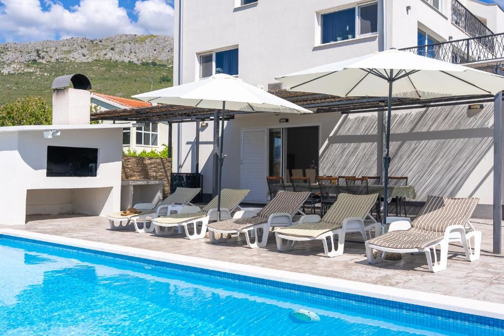 a pool with chairs and umbrellas next to a house at Modern apartment with private pool near Split in Podstrana