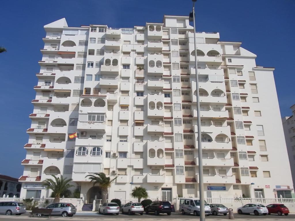 un edificio blanco alto con coches estacionados frente a él en Residencial Los Ibicencos V.v., en La Manga del Mar Menor