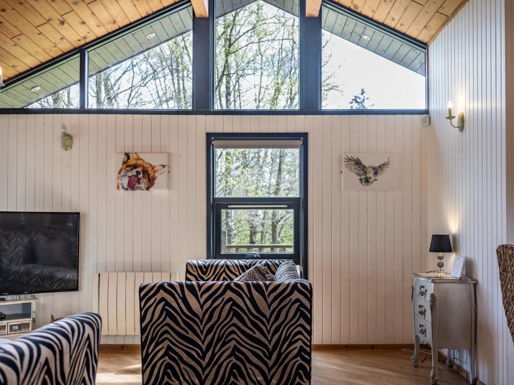 Luxury Cabin With Hot Tub and Sauna في أوتيربيرن: غرفة معيشة مع أريكة ذات طبعة حمار الوحشي ونوافذ