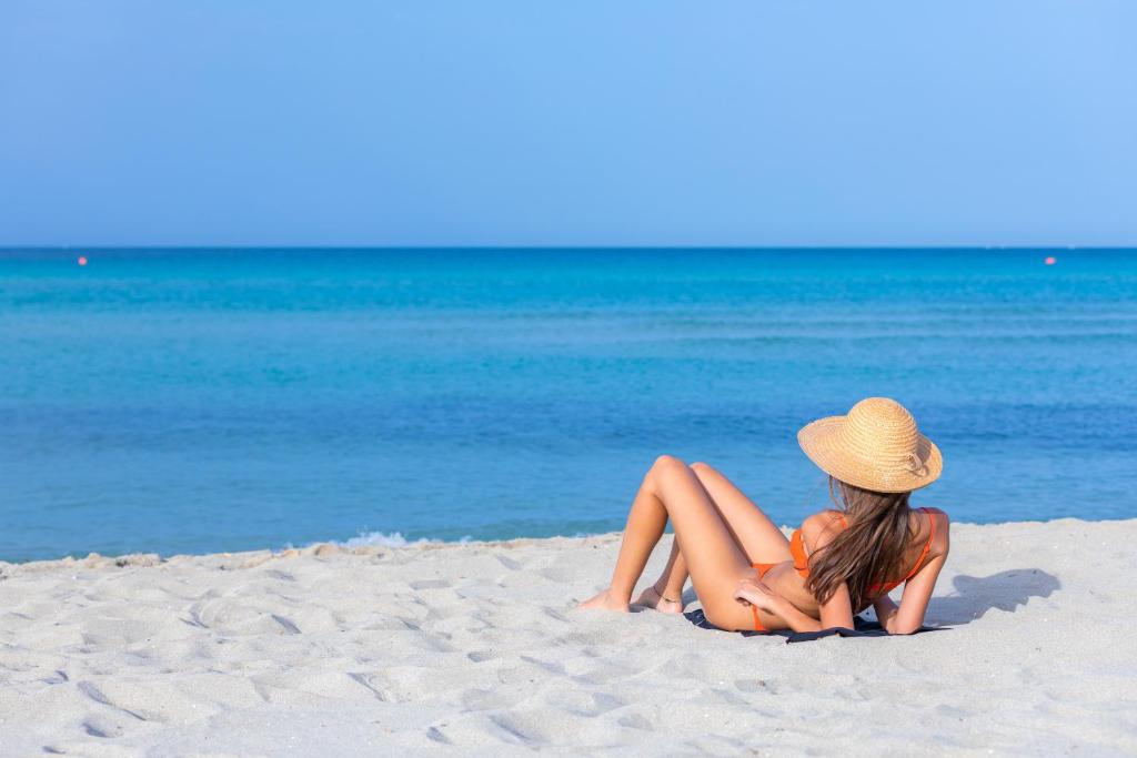 uma mulher de chapéu sentada numa praia em Riva di Ugento Beach Camping Resort em Ugento