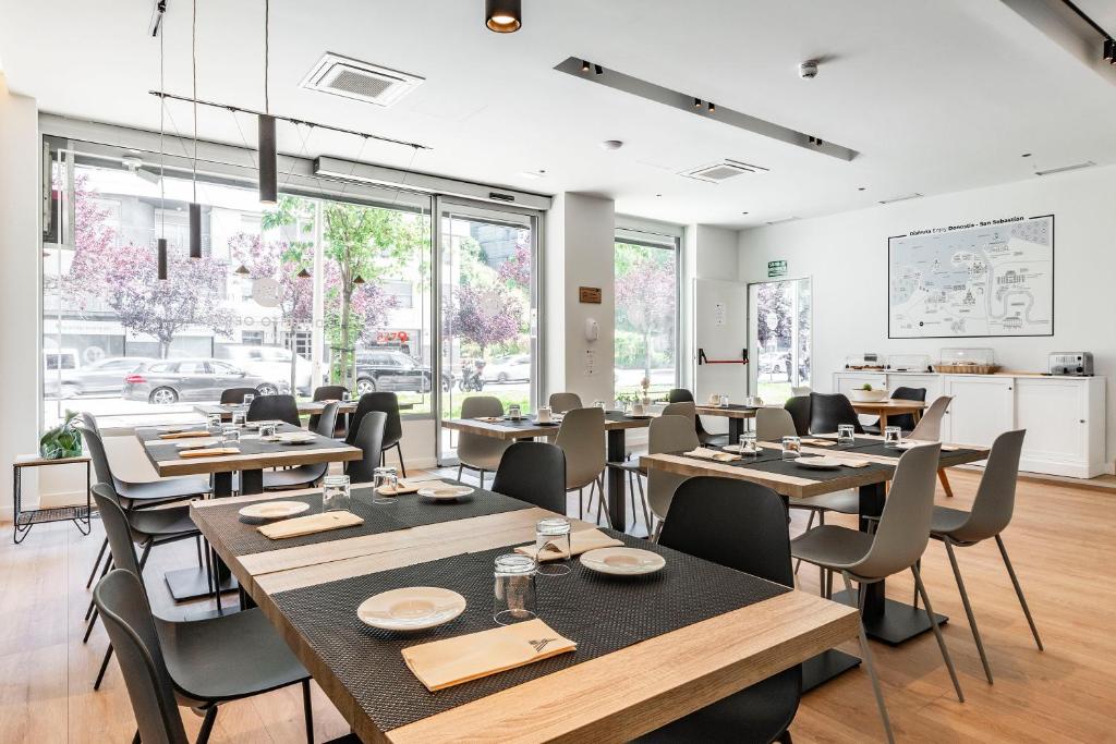 un restaurante con mesas y sillas de madera y ventanas en Hotel Distrito Oeste, en San Sebastián