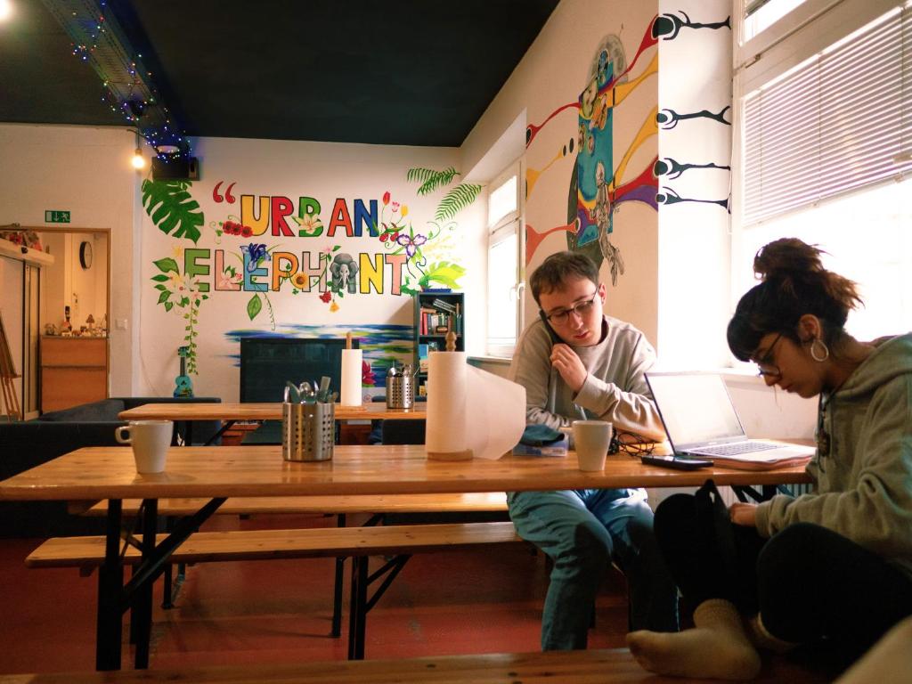 dos personas sentadas en una mesa con sus ordenadores portátiles en Urban Elephants Hostel en Bratislava