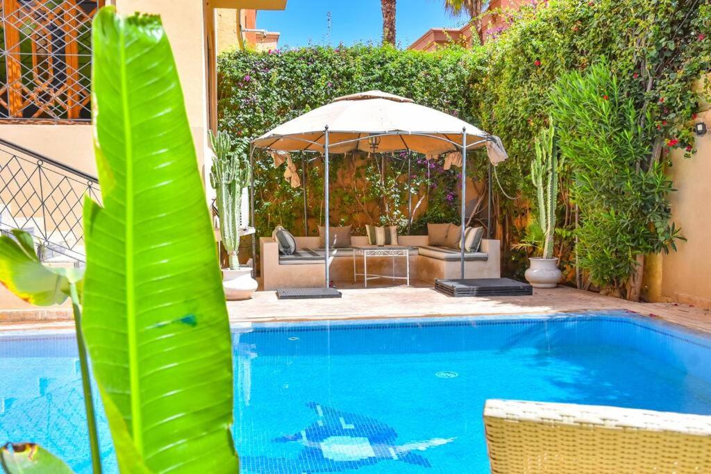 a swimming pool with an umbrella and chairs and a table at Villa in Central Marrakesh in Marrakech