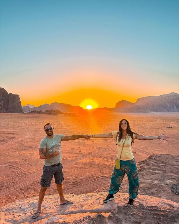 Un uomo e una donna in piedi davanti al tramonto di Rum Bright Moon Camp a Wadi Rum