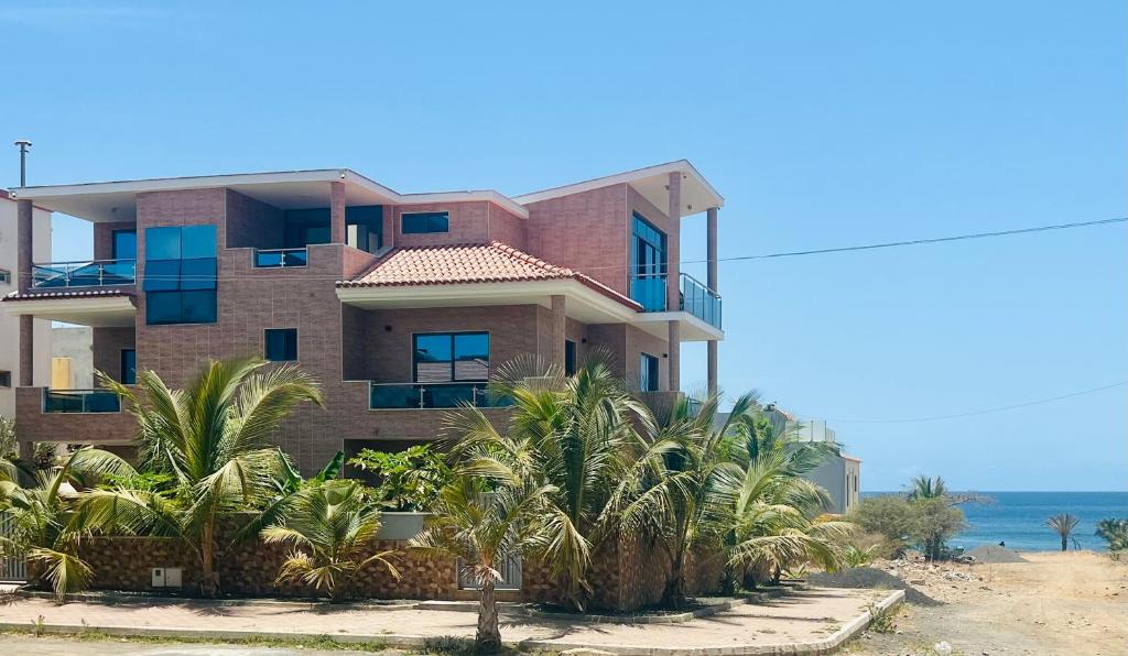 a building on the beach with palm trees in front at Lali's House in Tarrafal