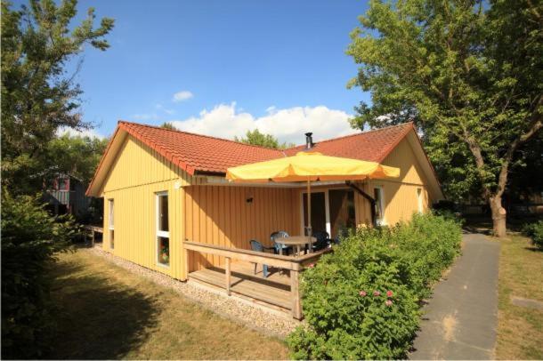 una pequeña casa amarilla con mesa y sombrilla en Möwe 14, en Mirow