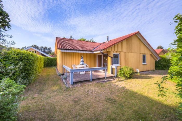 uma pequena casa amarela com um banco no quintal em Möwe 103 em Mirow