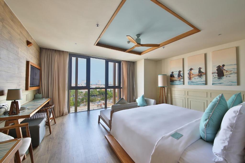 a hotel room with a bed and a desk and windows at Fusion Suites Vung Tau in Vung Tau