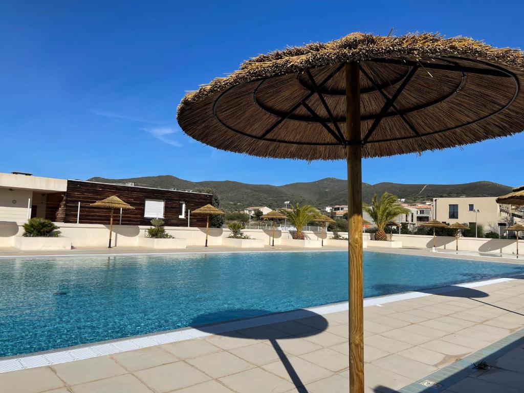 een grote parasol naast een zwembad bij Villa dans résidence avec piscines proche plage in Belgodère