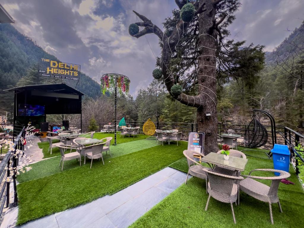 um jardim com mesas e cadeiras e uma árvore em Delhi Height Kasol - Cafe and Hotel em Kasol