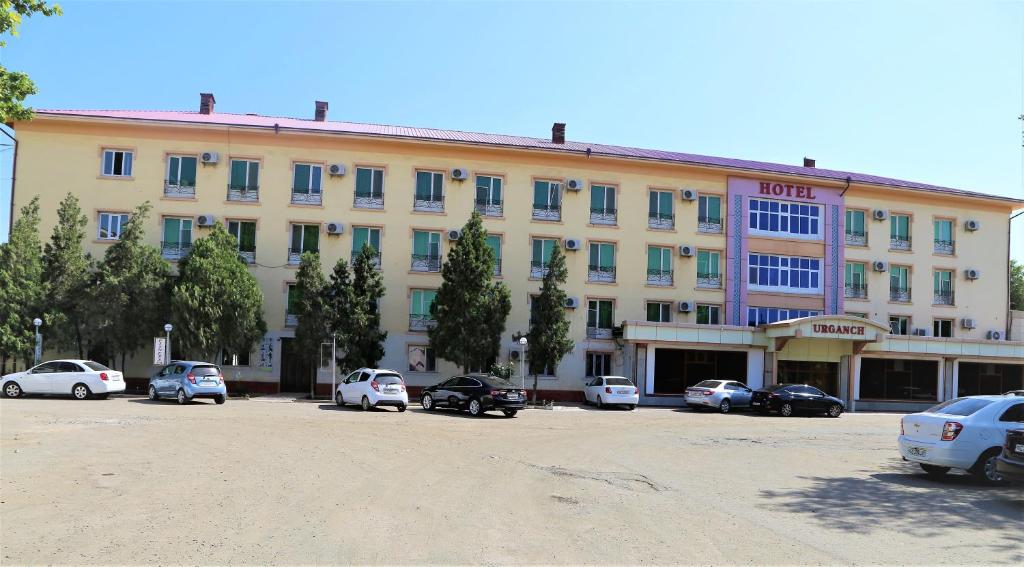 ein großes Gebäude mit Autos auf einem Parkplatz in der Unterkunft URGANCH Hotel in Urganch