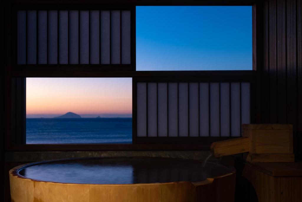 a room with a tub in front of two windows at Isoaruki no Yuyado Ushiogumo -6 years or older- in Kawazu