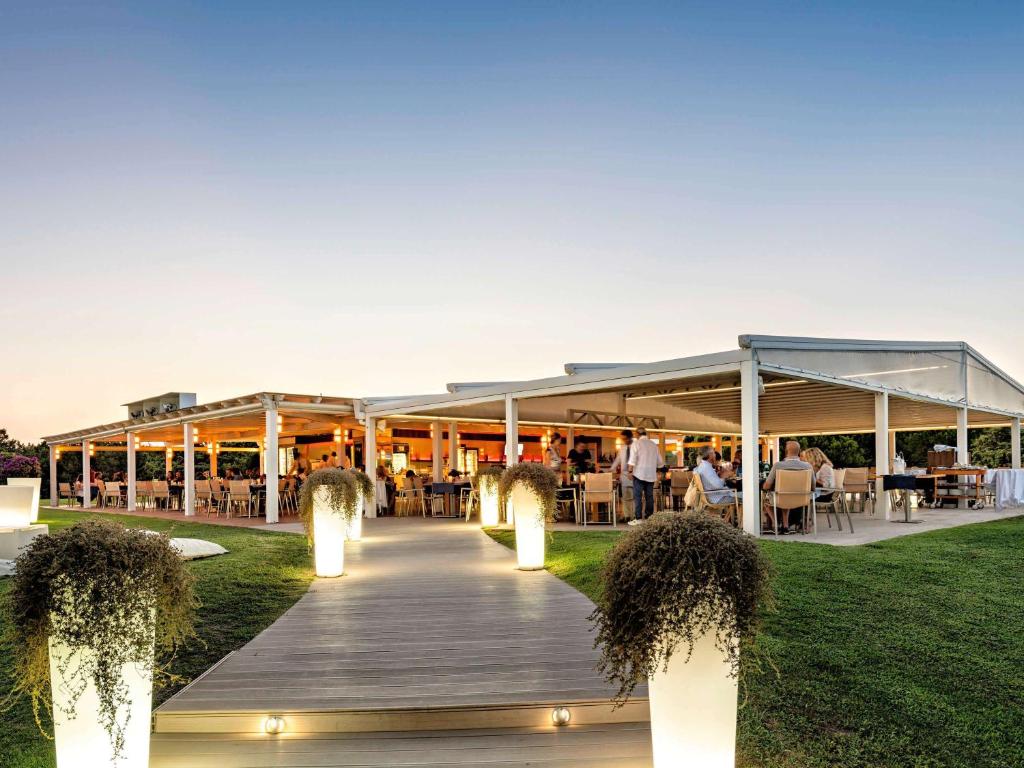 a boardwalk leading to a restaurant with people sitting at tables at Almar Timi Ama Resort & Spa in Villasimius