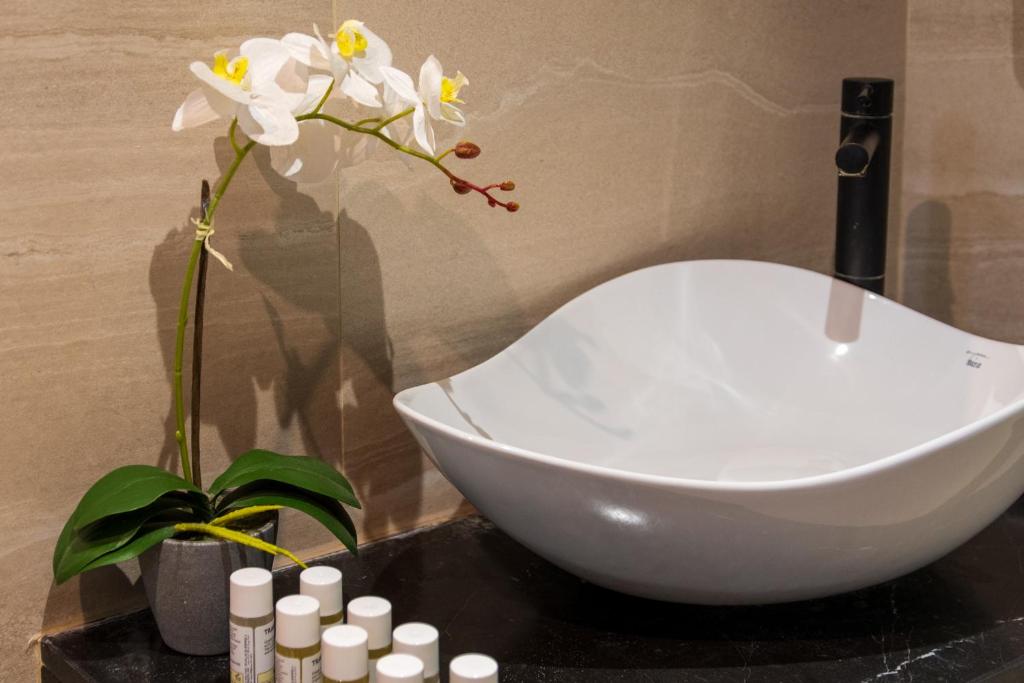 a white bowl on a table with a vase with flowers at Malena Hotel & Suites - Adults Only by Omilos Hotels in Amoudara Herakliou