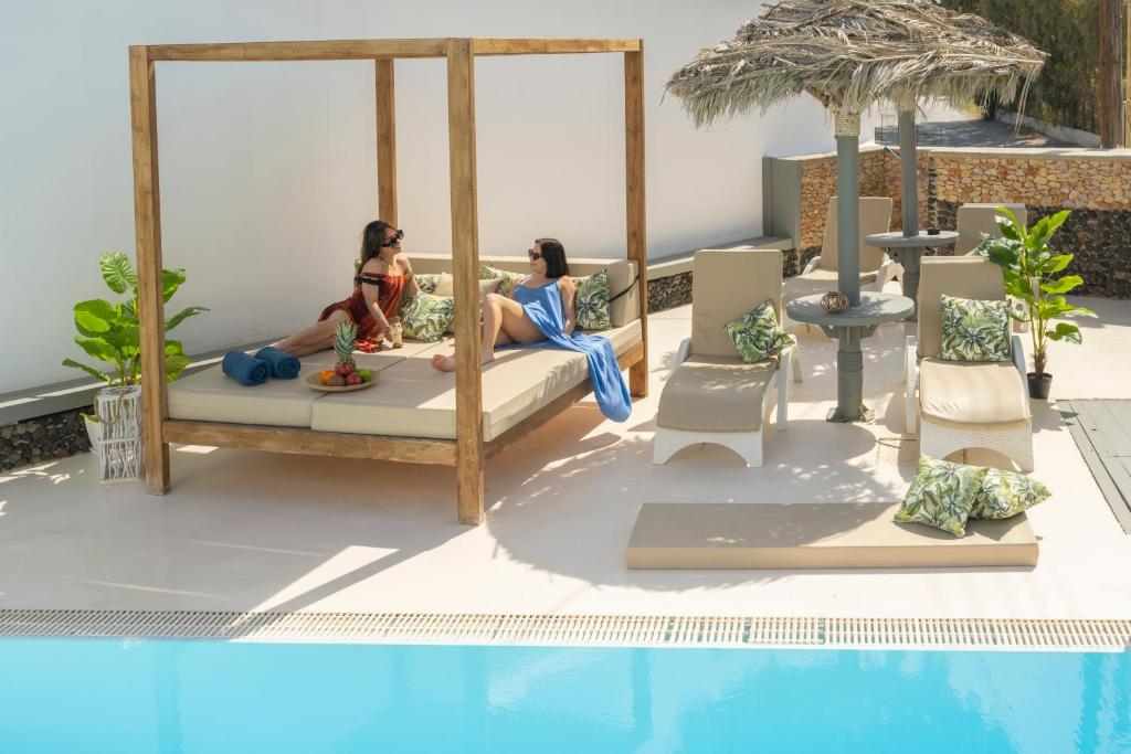 two women sitting on a bed next to a swimming pool at Loukas & Emma Eco Houses in Perissa
