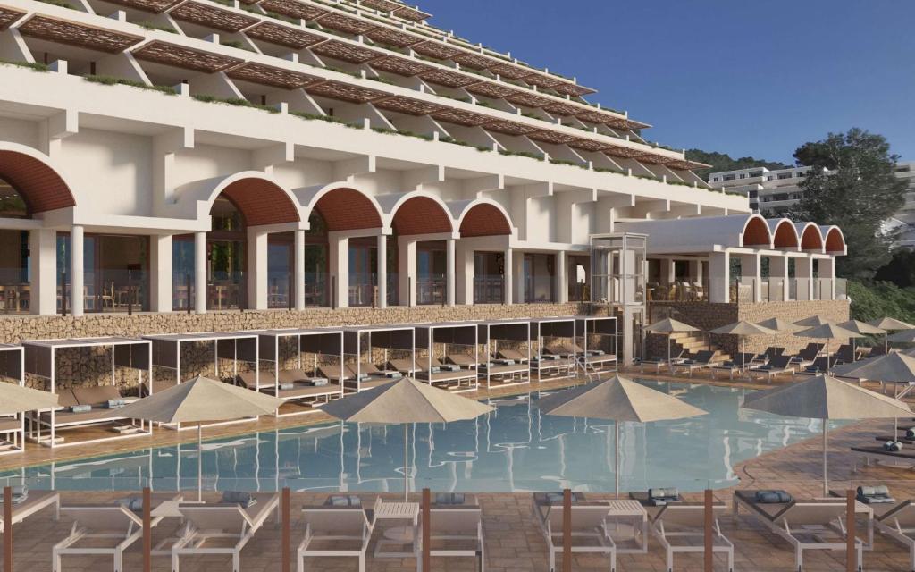 basen z leżakami i parasolami przed budynkiem w obiekcie Cala San Miguel Hotel Ibiza, Curio Collection by Hilton, Adults only w mieście Puerto de San Miguel