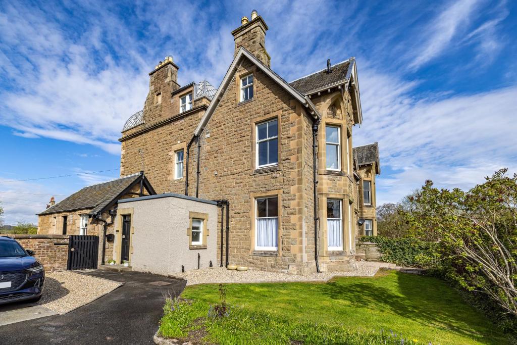 una gran casa de ladrillo con un coche aparcado en la entrada en Lower Tweedknowe - ground floor villa Melrose en Melrose