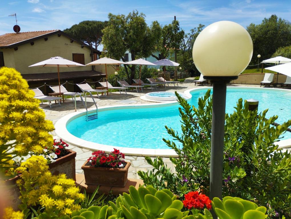 a swimming pool with chairs and umbrellas and flowers at Agriturismo La Luciana in Castiglione della Pescaia