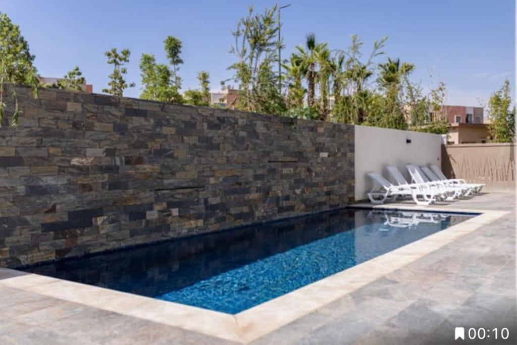 einen Pool mit Stühlen neben einer Backsteinmauer in der Unterkunft Villa panorama in Marrakesch