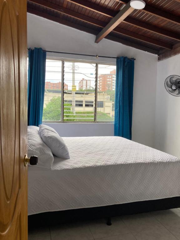 a bedroom with a bed with blue curtains and a window at Hotel Mallorca Estadio, Medellin in Medellín