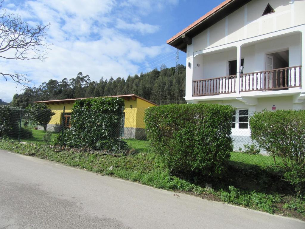 Una casa blanca y amarilla con arbustos al lado de una calle. en Casa Pita, en Bárcena de Cicero