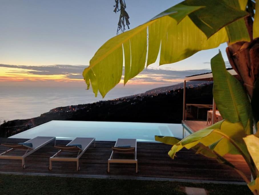 a pool with chairs and a view of the ocean at Villa Amendoa in Arco da Calheta