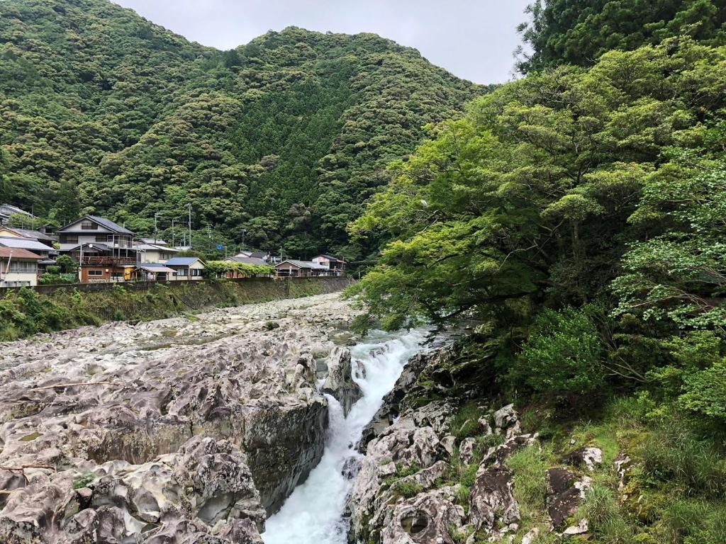 a river flowing down a rocky hillside with houses at ラコマハウス古座川古民家一棟貸し in Takinohai
